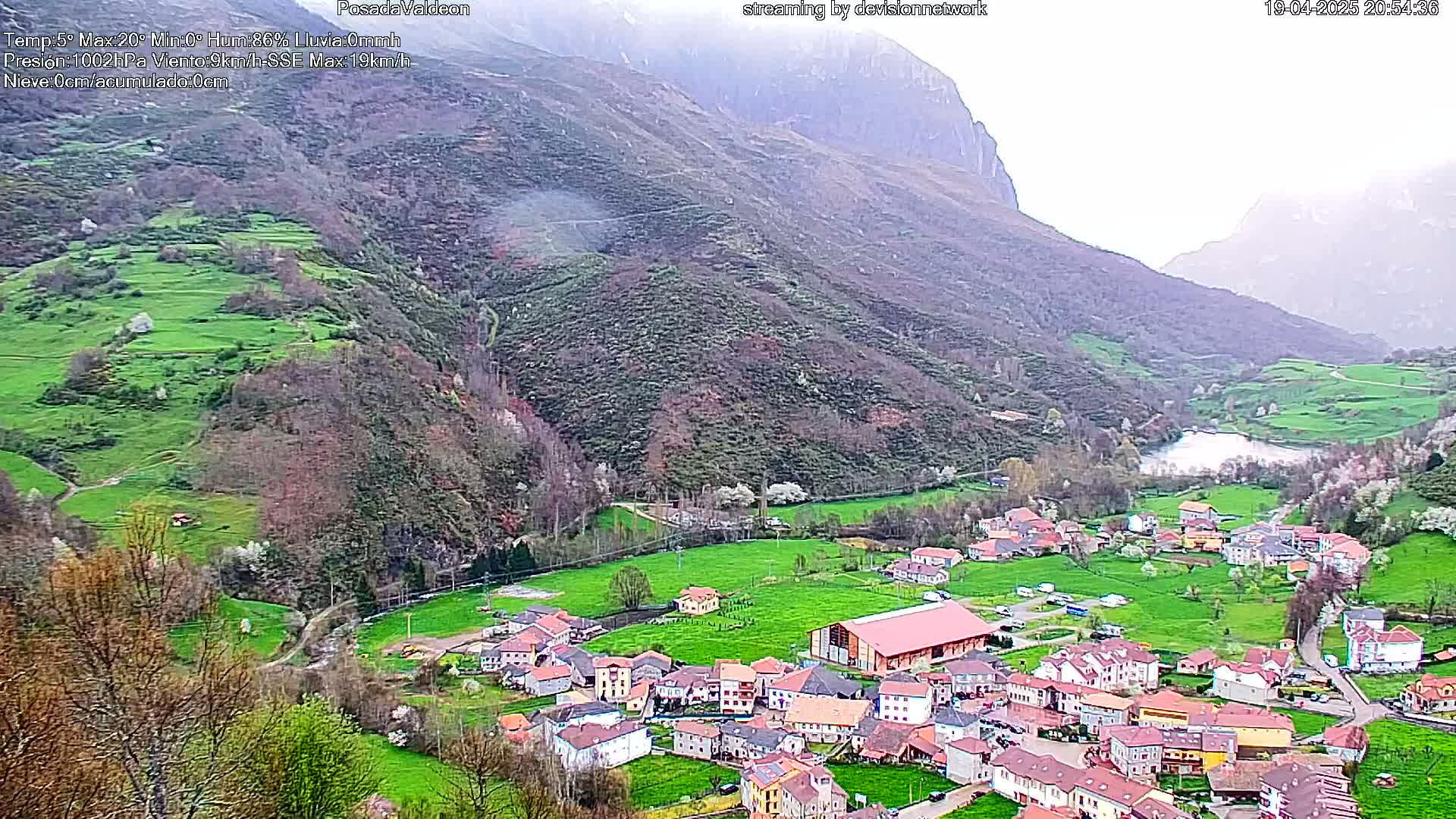 A small village nestled in a verdant valley between mountains, under overcast skies.