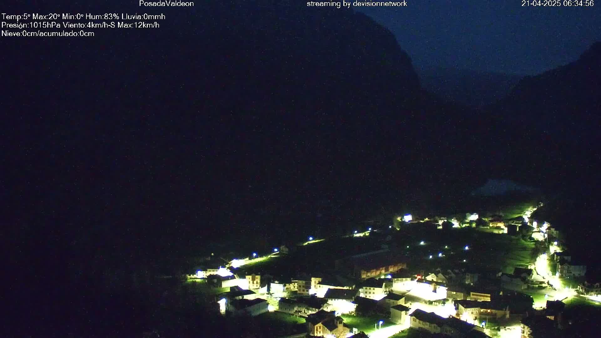 A small village nestled in a valley at night, illuminated by lights, with dark mountains in the background under a clear, dark sky.