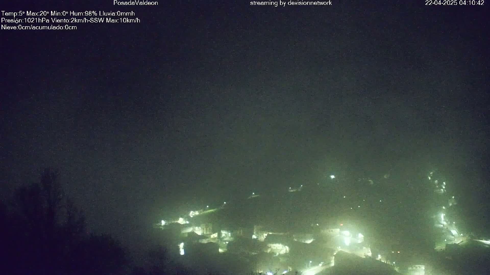 A nighttime view of a village shrouded in fog, with faint lights visible from buildings.