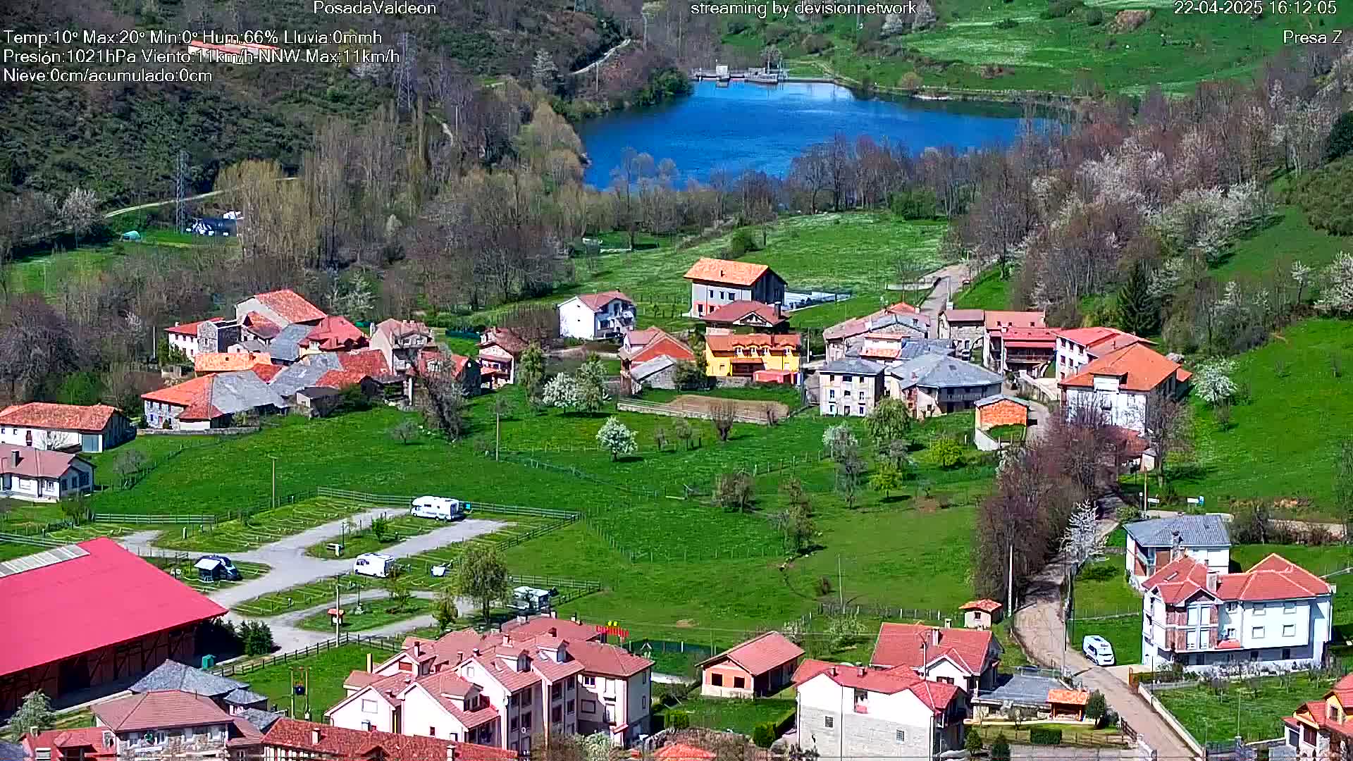 A small village nestled in a verdant valley next to a calm lake under a sunny sky.