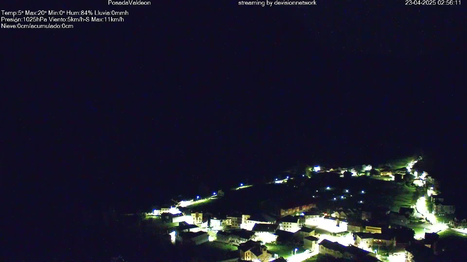 A nighttime aerial view of a small, illuminated town nestled in a dark, hilly landscape under a clear, starless sky.