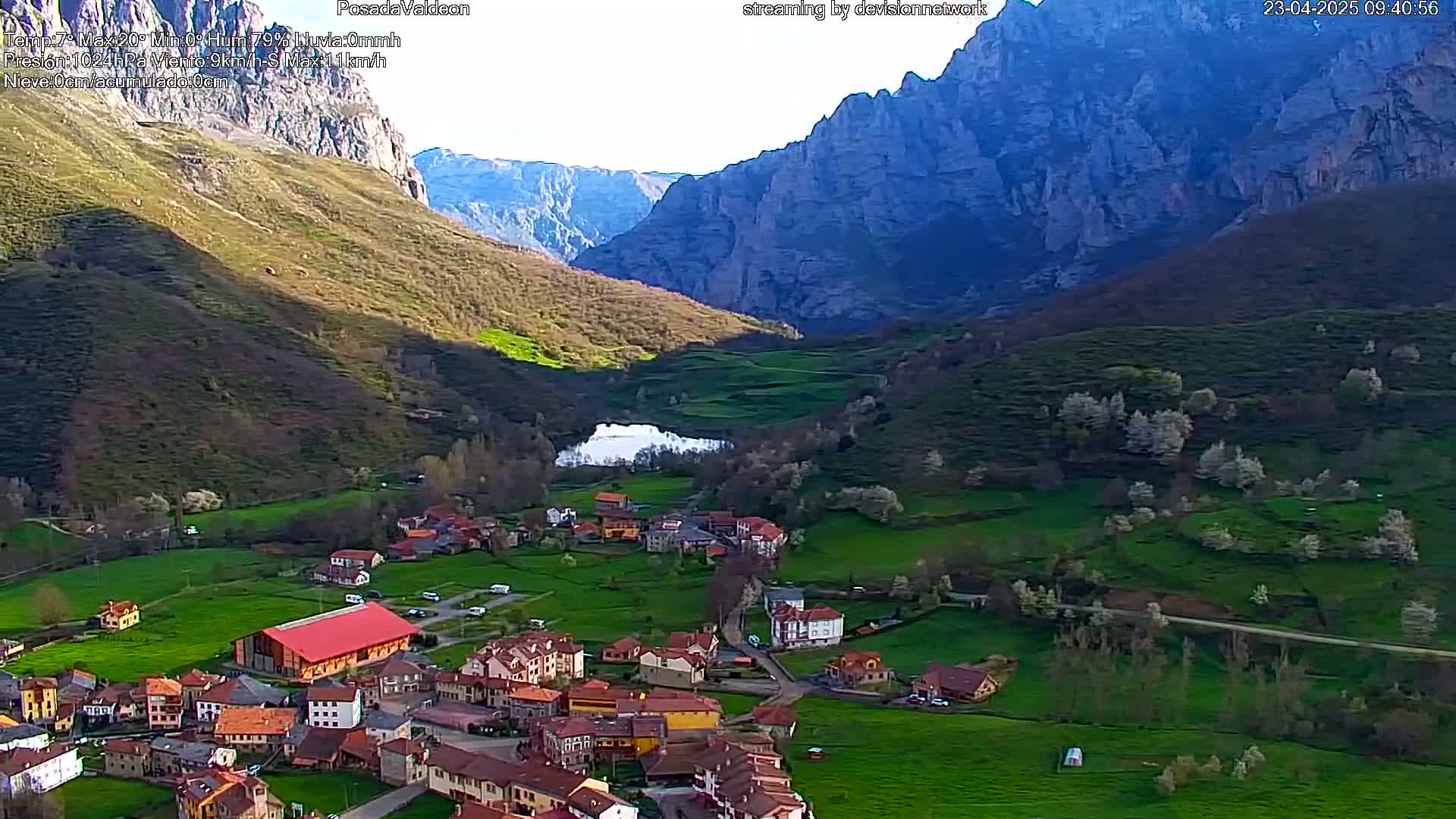 A small village nestled in a verdant valley between towering mountains, under a clear sky.