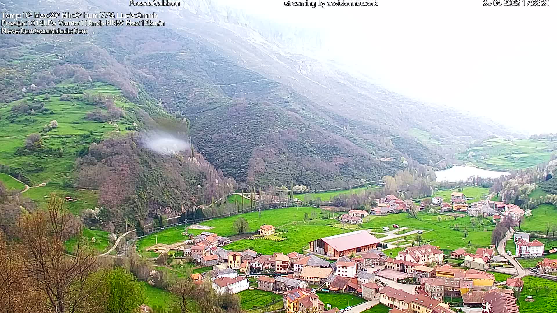 A small village nestled in a verdant valley, surrounded by mountains under an overcast sky.