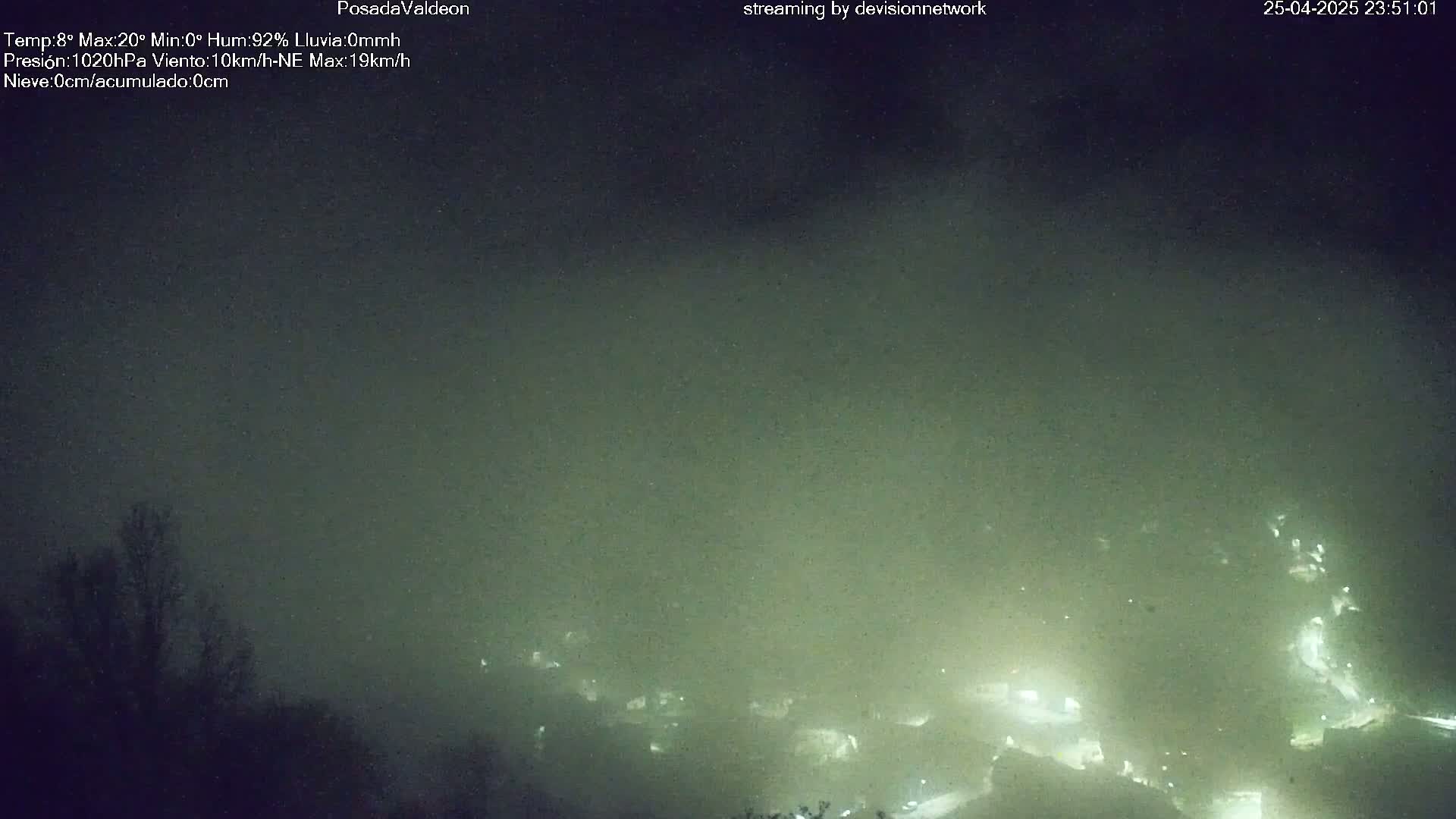 A nighttime view of dimly lit buildings and trees shrouded in heavy fog.