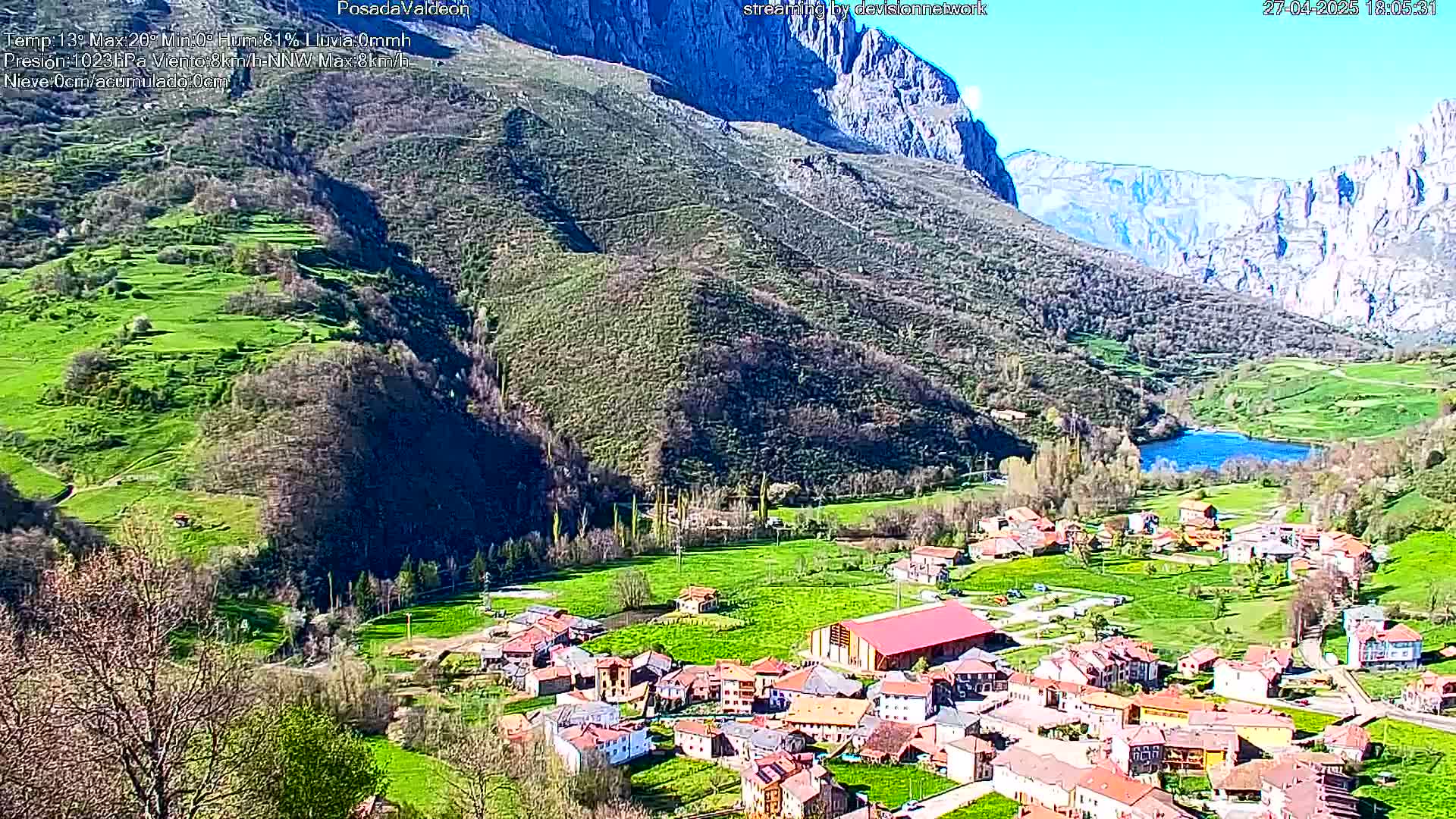 A small village nestled in a verdant valley, surrounded by mountains under a clear blue sky.