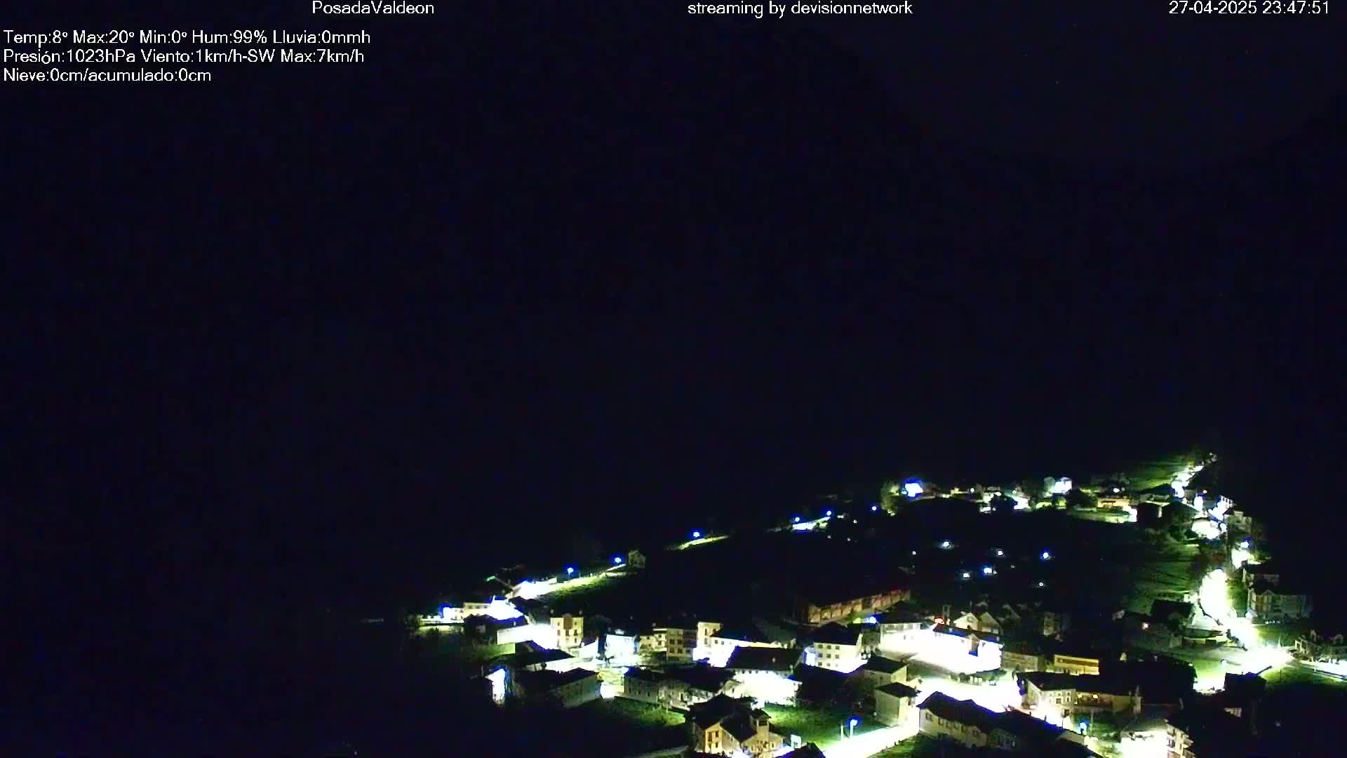 A small, illuminated town is nestled in a dark, nighttime landscape under a clear, dark sky.