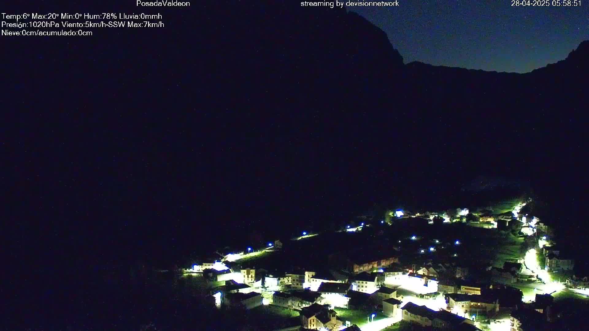 At night, a small village nestled in a valley below a dark mountain is illuminated by lights.