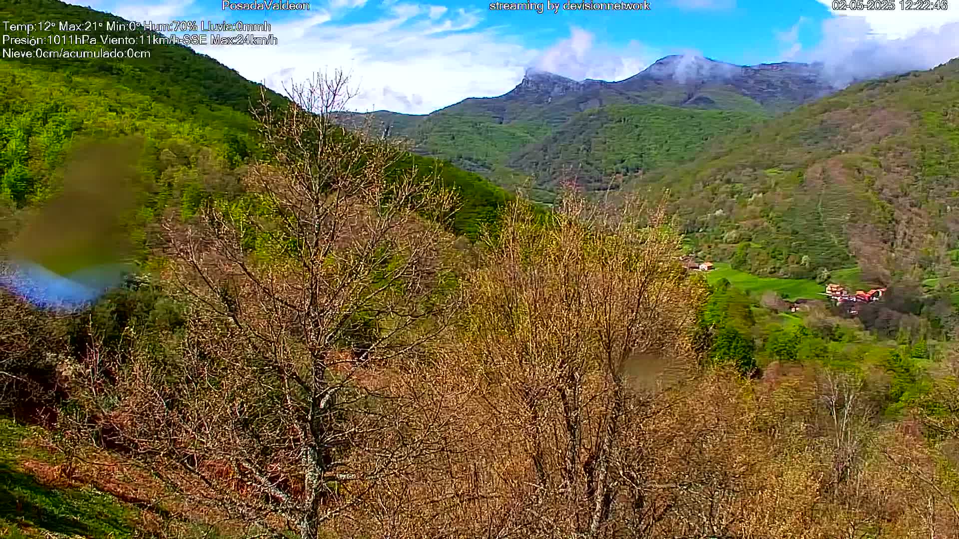 A partly cloudy day reveals a valley of budding trees and distant mountains partially shrouded in mist.