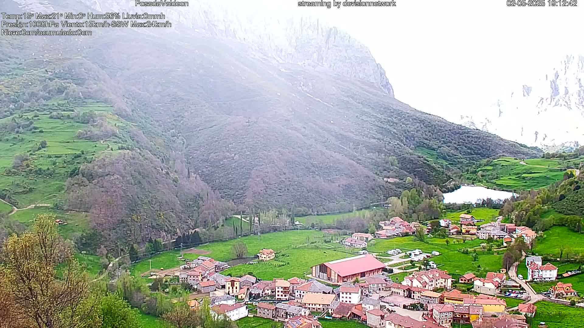 A small village nestled in a verdant valley, bordered by mountains under a slightly hazy sky.