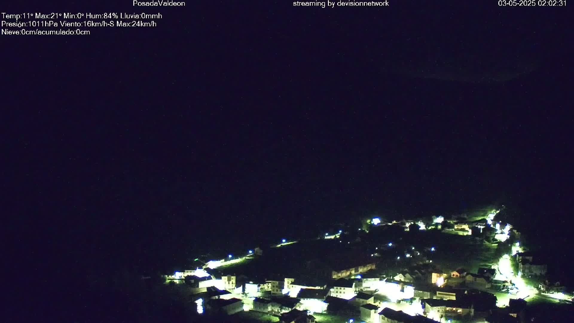 A small, illuminated village is nestled in a dark, nighttime landscape.
