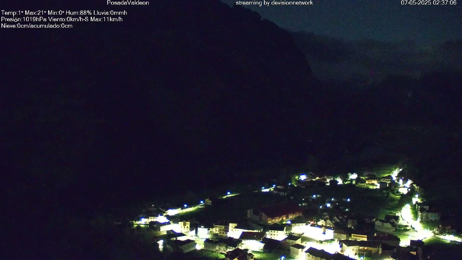 A small, dark village nestled in a valley at night, illuminated by scattered lights, under a dark, cloudy sky.