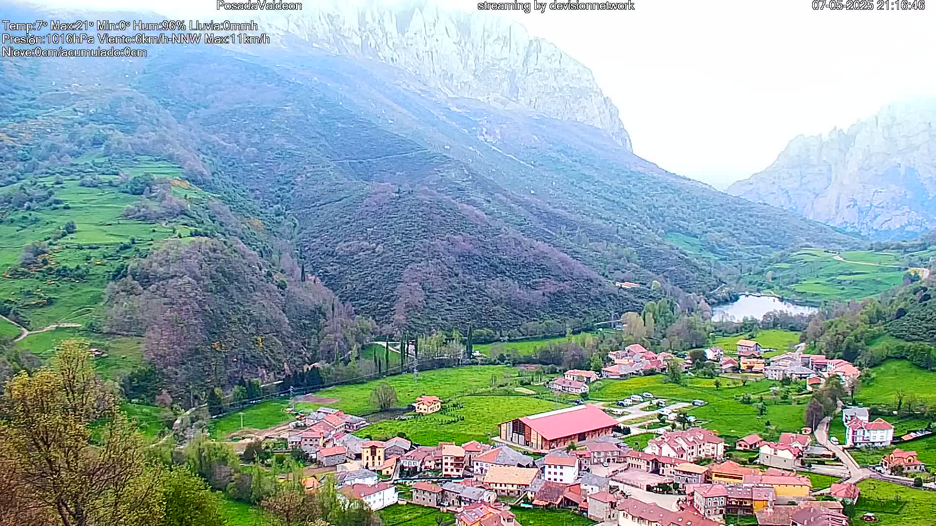 A small village nestled in a verdant valley between towering mountains under an overcast sky.