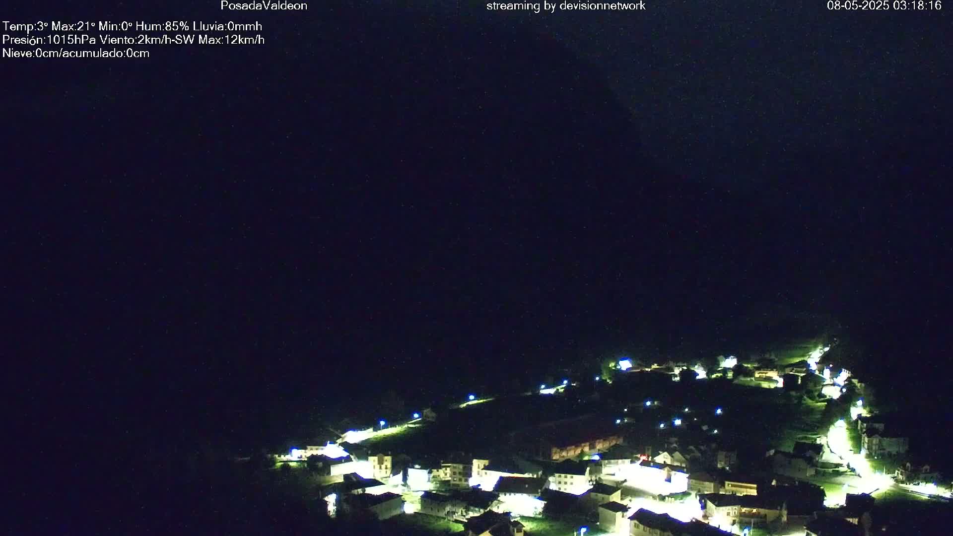 A nighttime view of a small, illuminated village nestled in a dark, hilly landscape under a clear, dark sky.