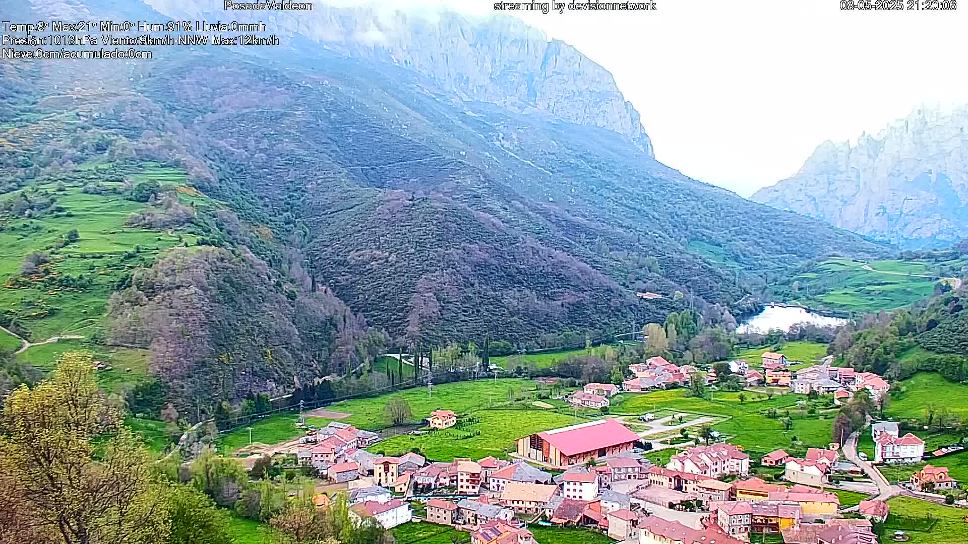 A small village nestled in a verdant valley between steep, rocky mountains under a hazy sky.