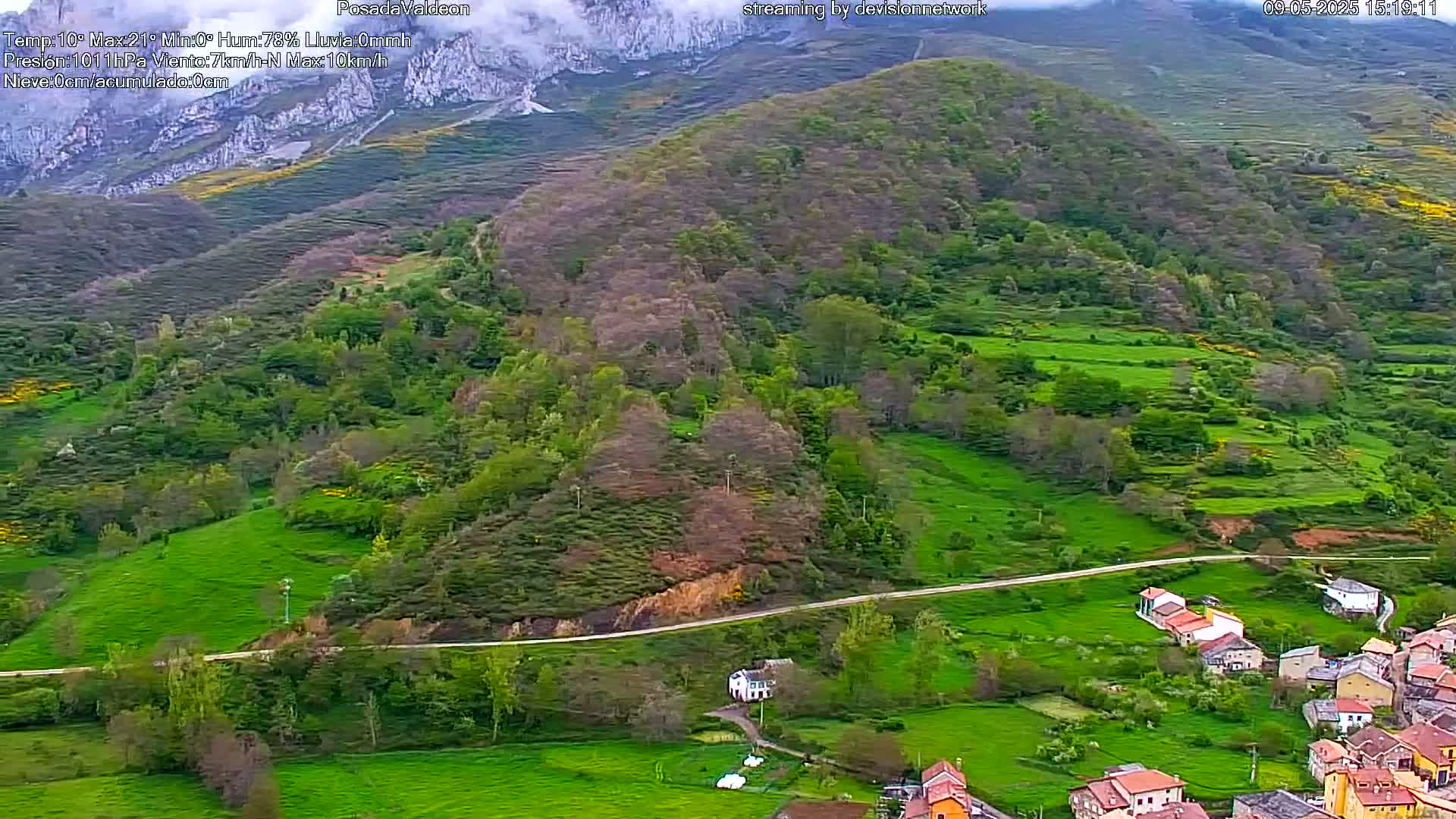 A hilly landscape, dotted with green fields and a small village, stretches beneath a partly cloudy sky.