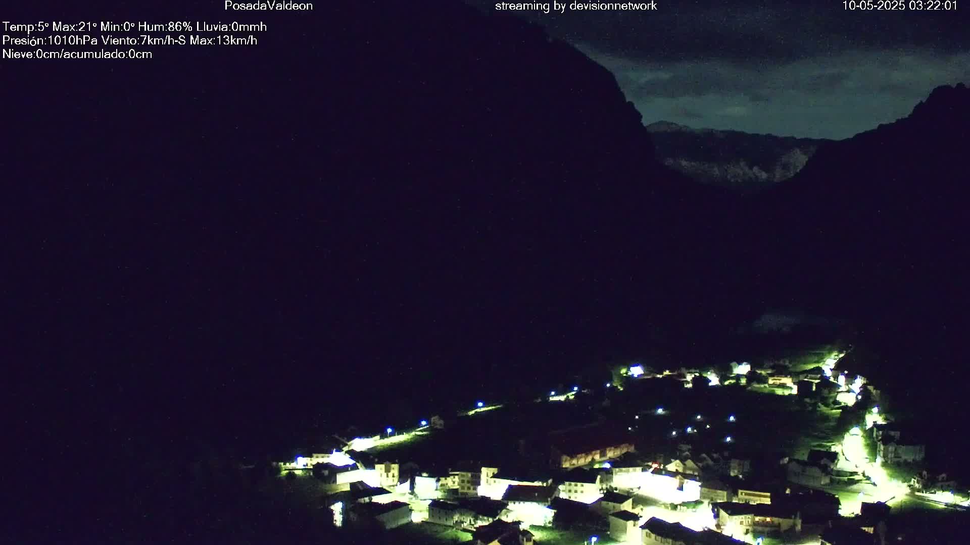 A nighttime view of a small village nestled in a valley between dark mountains under a mostly clear sky.