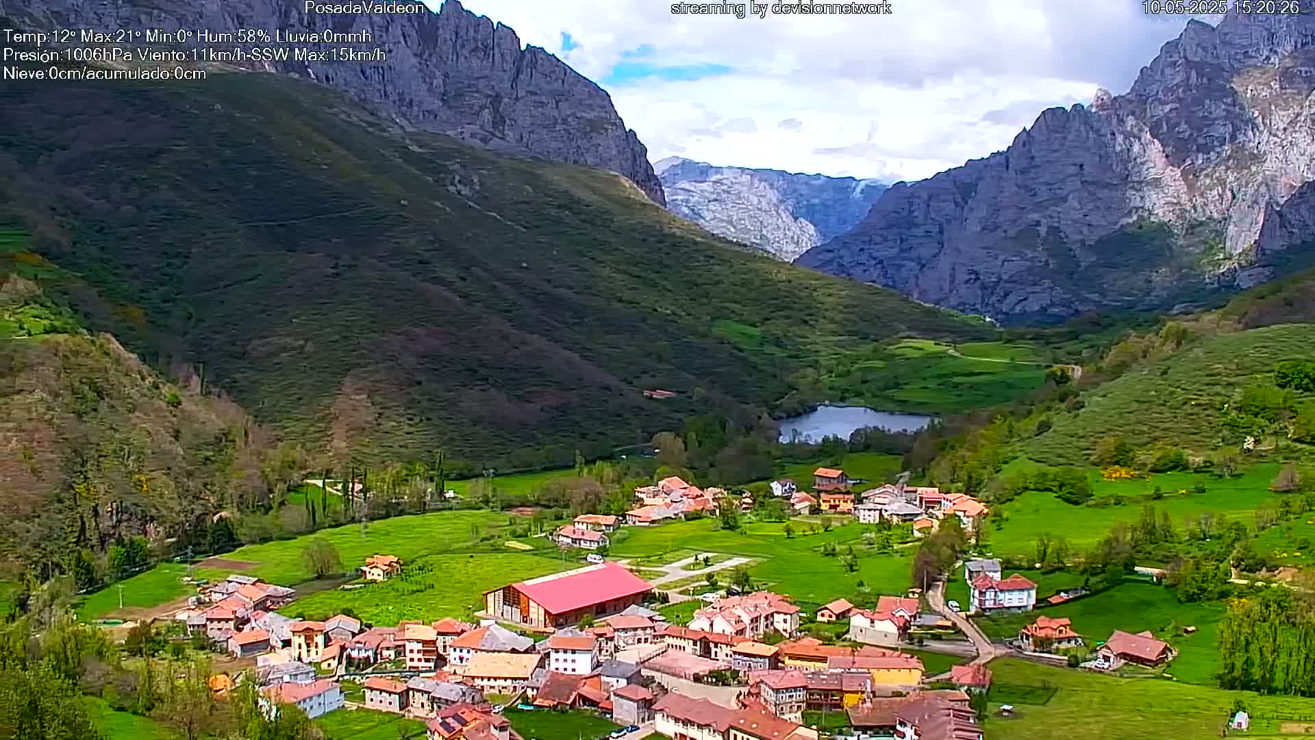 A small village nestled in a verdant valley between towering mountains under partly cloudy skies.