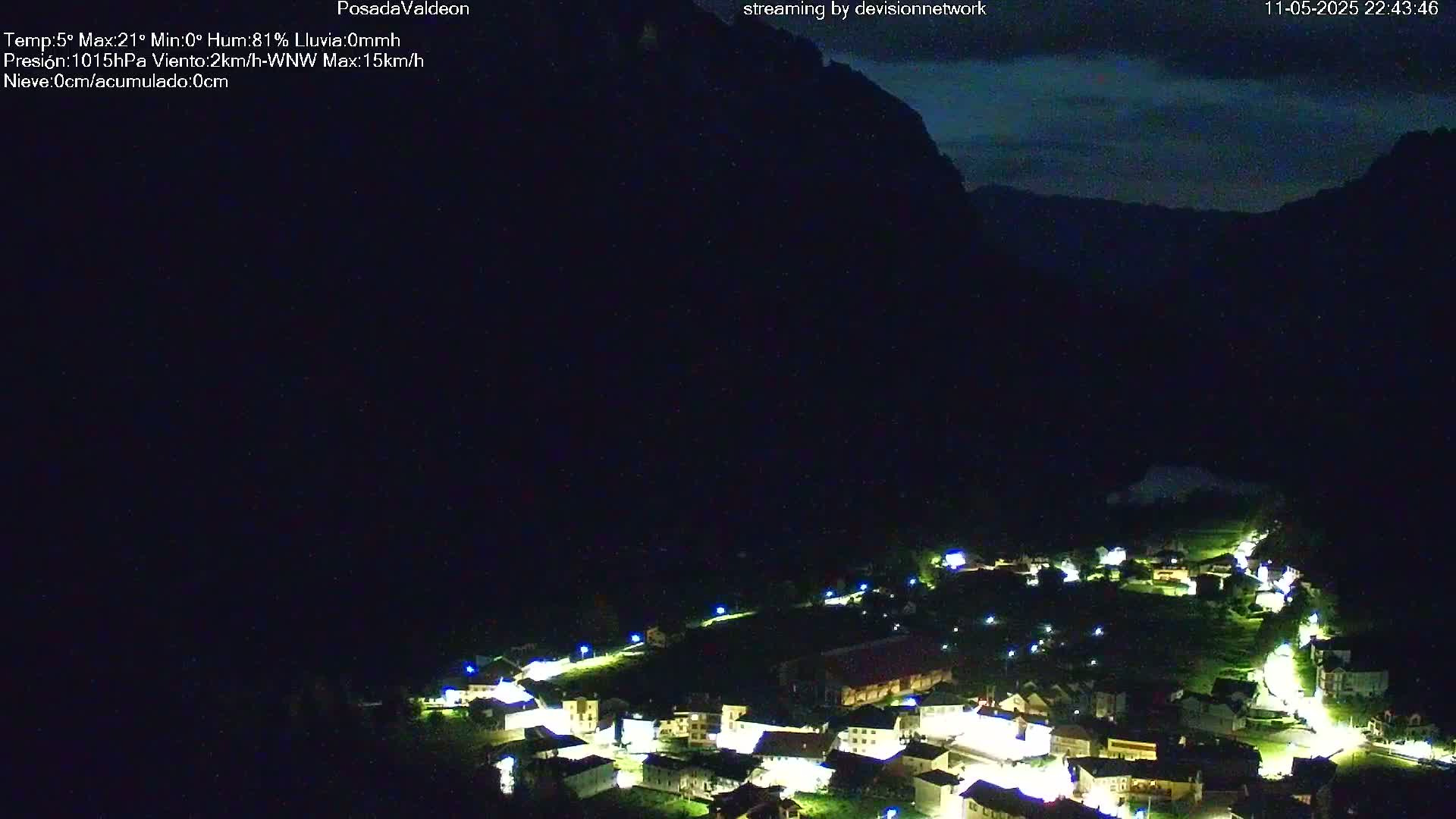 A nighttime, high-angle view shows a small village illuminated in a valley nestled beneath dark mountains under a mostly clear night sky.