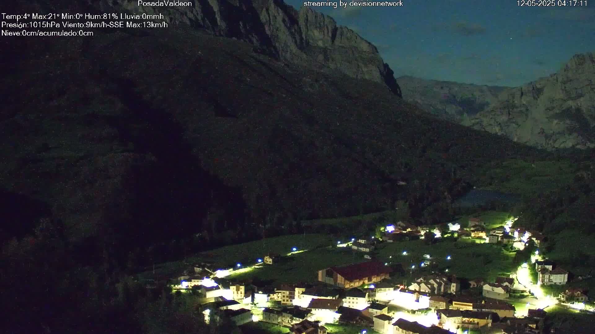 A small village nestled in a valley at night, illuminated by lights, under a dark, clear sky with a mountain looming in the background.