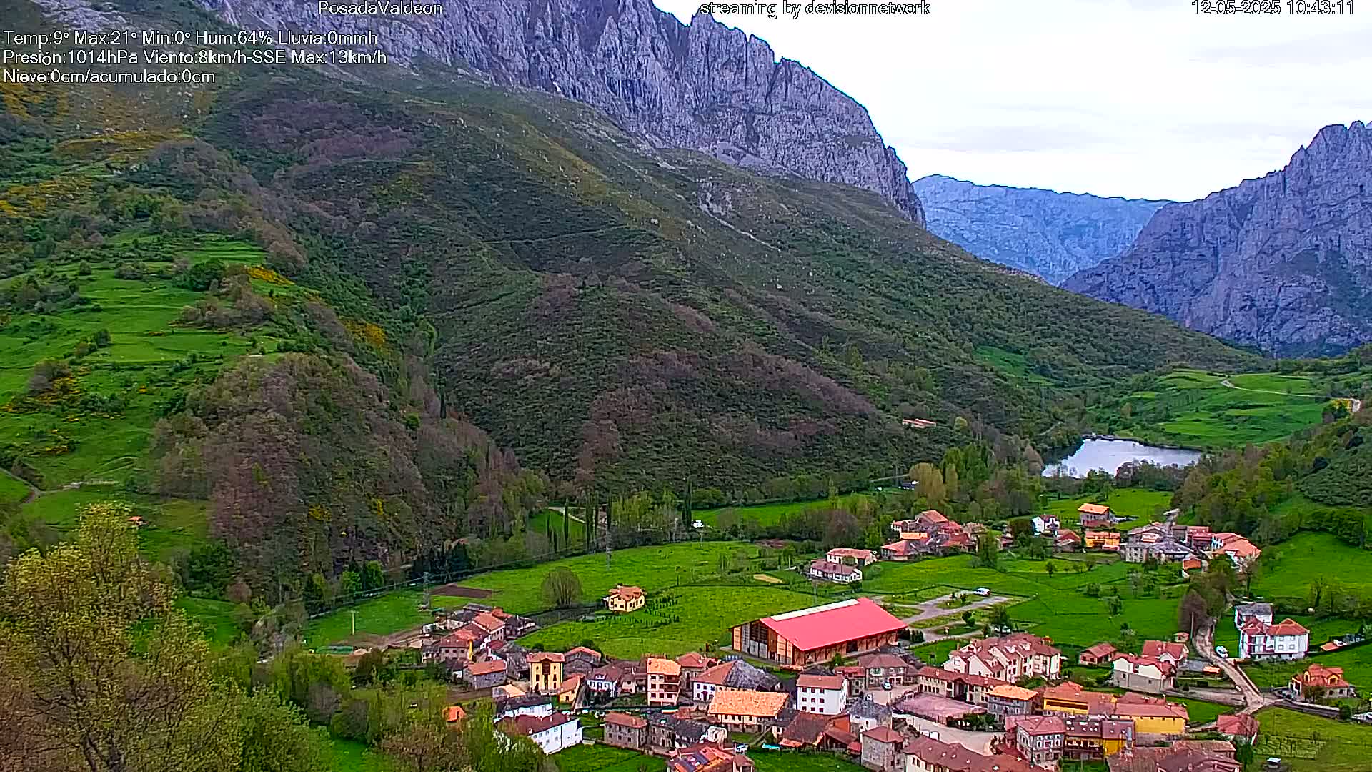 A small village nestled in a verdant valley between imposing, rocky mountains, under an overcast sky.