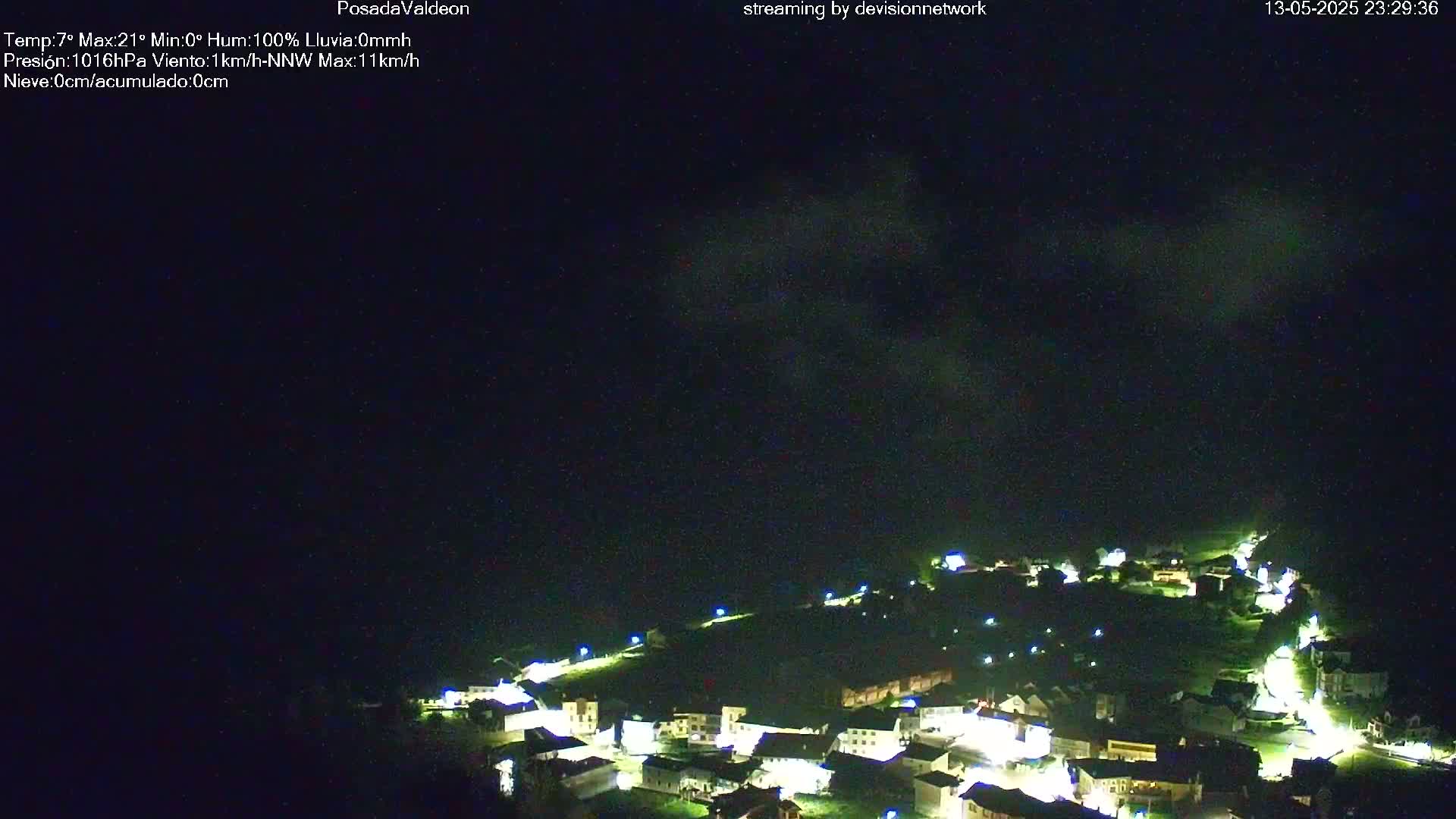 A small, illuminated village nestled on a hillside under a dark, cloudy night sky.