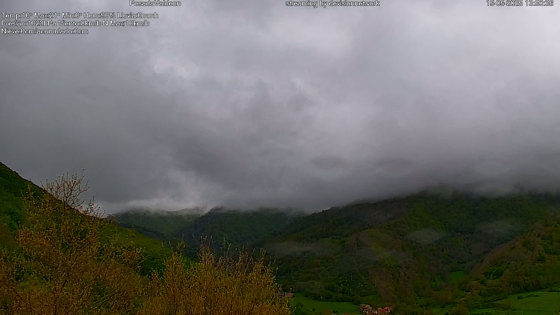A low-hanging cloud cover obscures a valley of green hills and trees under an overcast sky.