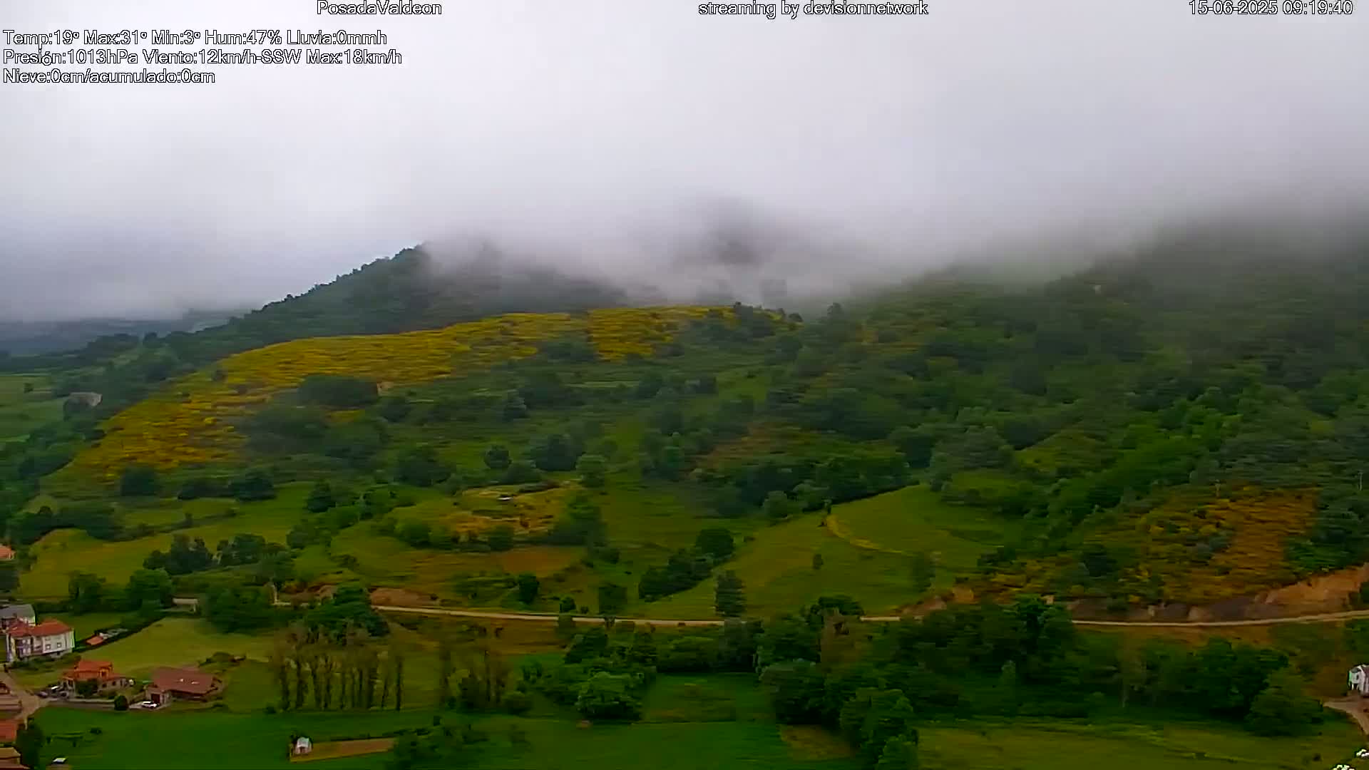 A foggy, hilly landscape with green fields and trees, a small village nestled at its base.