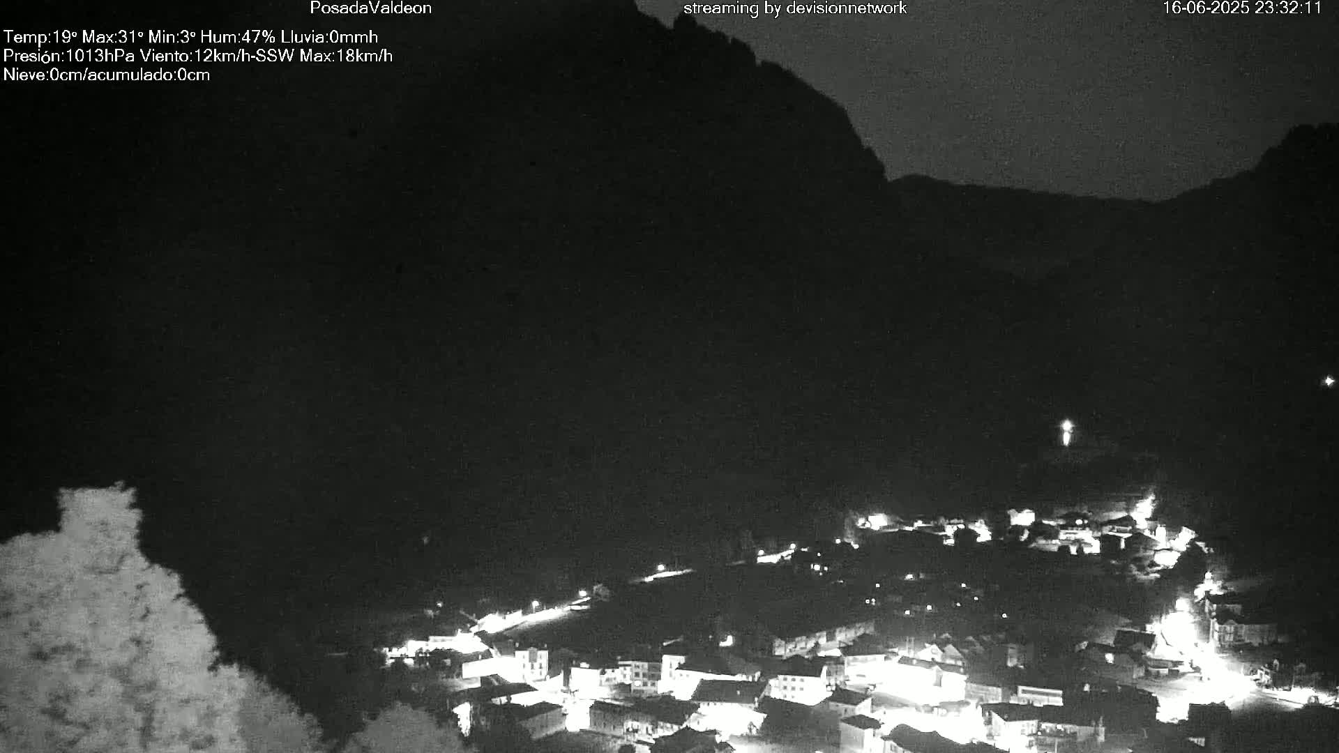A nighttime, low-light view of a small town nestled at the base of a dark mountain, under a clear sky.