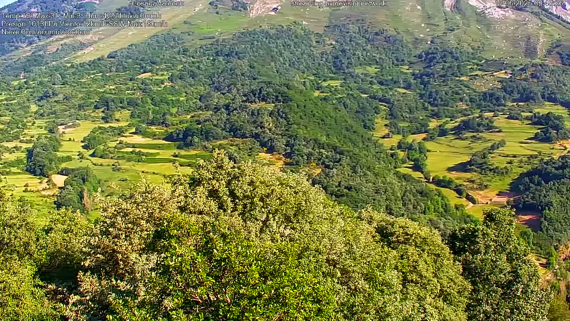A sunny view of a verdant valley with patches of farmland, nestled amongst rolling hills and lush green forests.