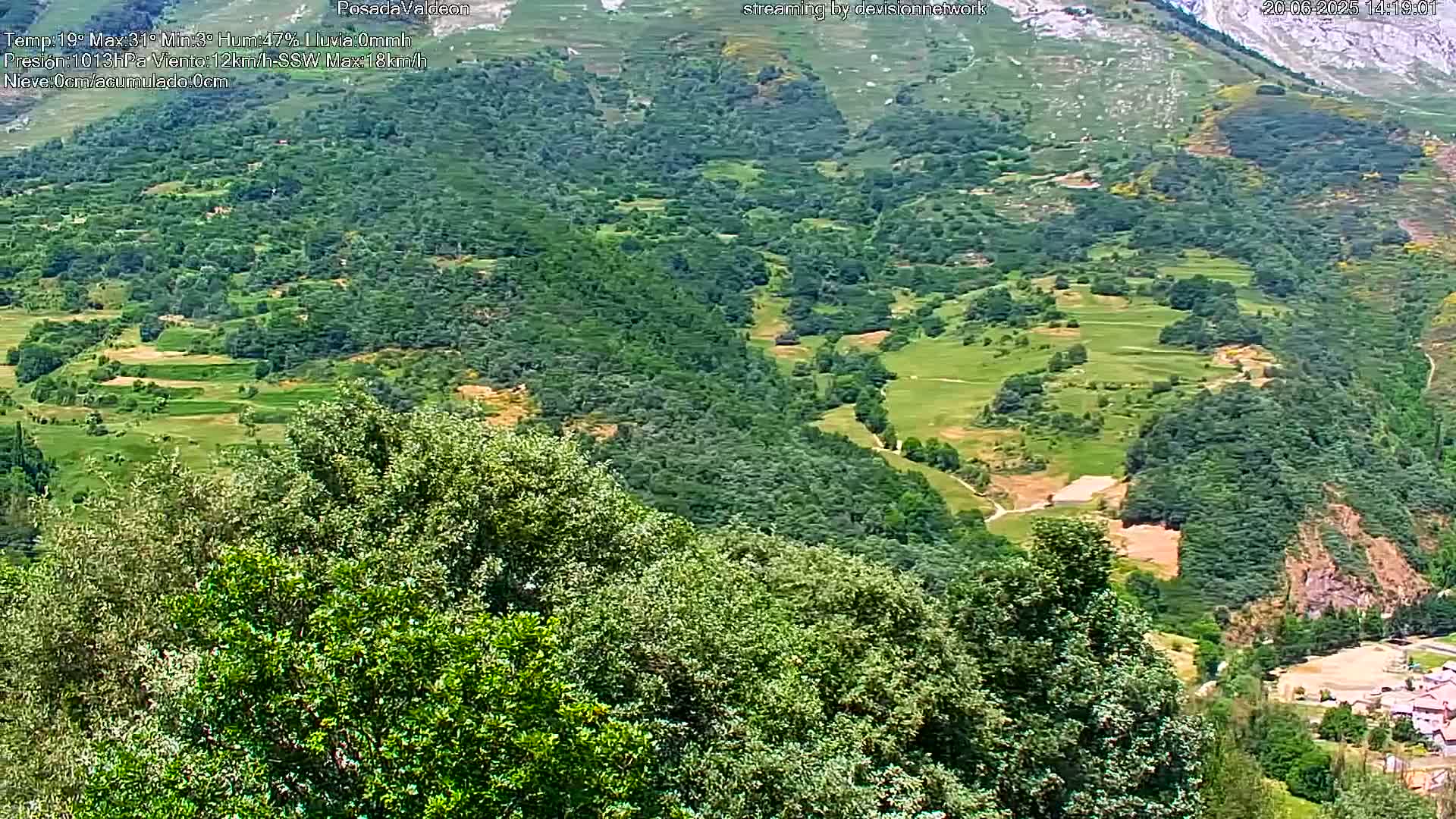 A lush green valley dotted with patches of farmland and trees stretches toward distant mountains under a clear sky.