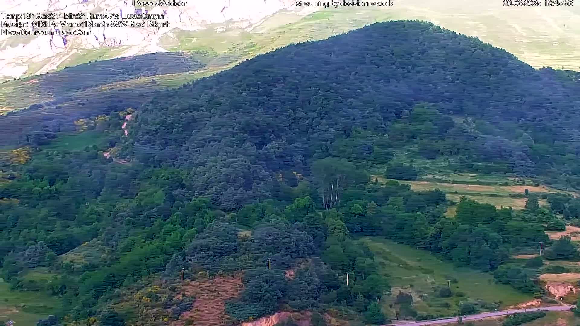 A lush green mountainside, partially forested and partially cleared, is visible under a clear sky.