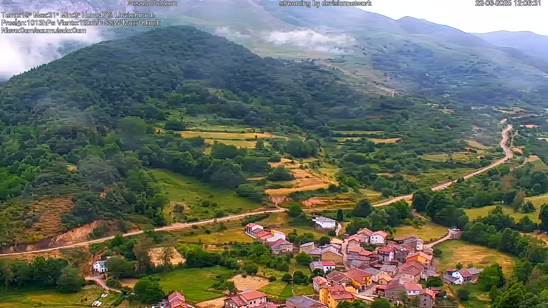 A small village nestled in a verdant valley, surrounded by rolling hills and mountains partially shrouded in mist.