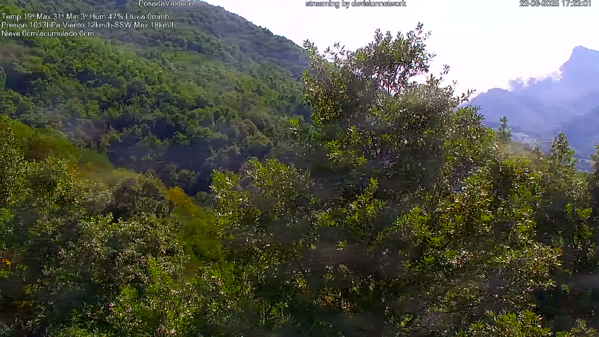 Lush green vegetation covers a hillside and valley, with distant mountains visible under a mostly clear sky.