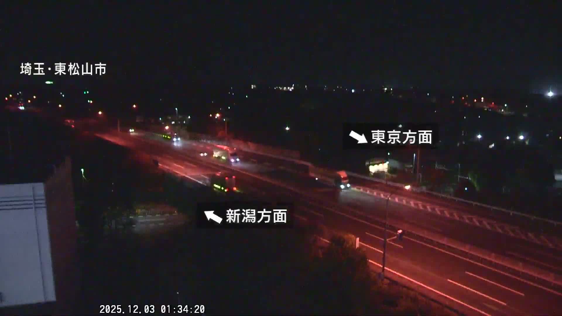 An overhead nighttime view captures a multi-lane highway with various vehicles, including trucks, illuminated by streetlights and vehicle lights under clear skies.