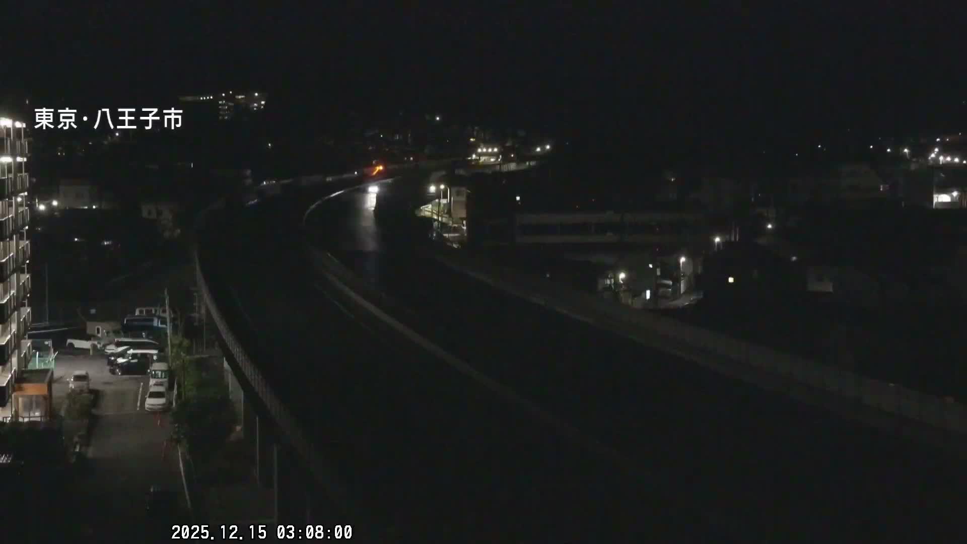 The image displays an elevated highway at night with visible vehicle headlights and taillights, surrounded by illuminated buildings and city lights under clear weather conditions.