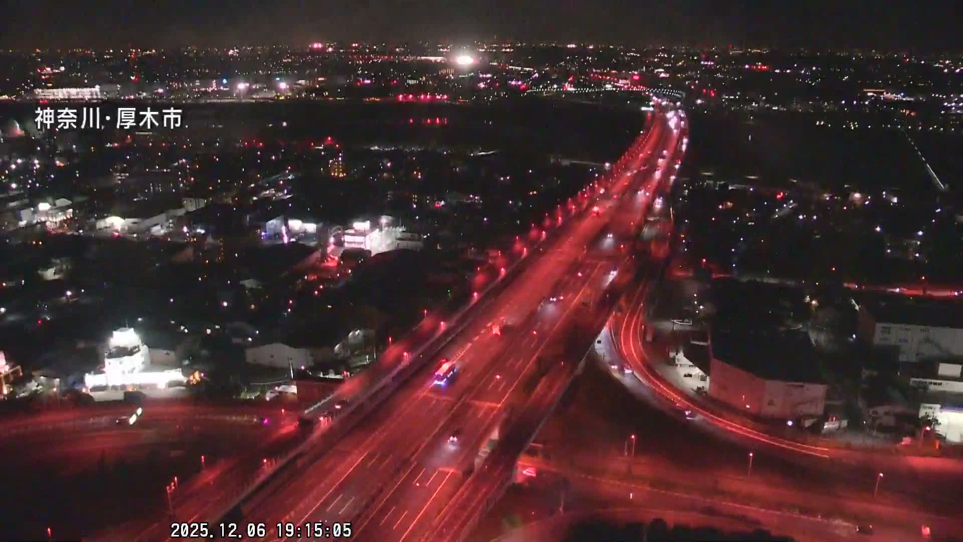 An aerial night view depicts a bustling city with prominent red-lit highways carrying vehicles, surrounded by numerous city lights fading into the distance under a clear night sky.