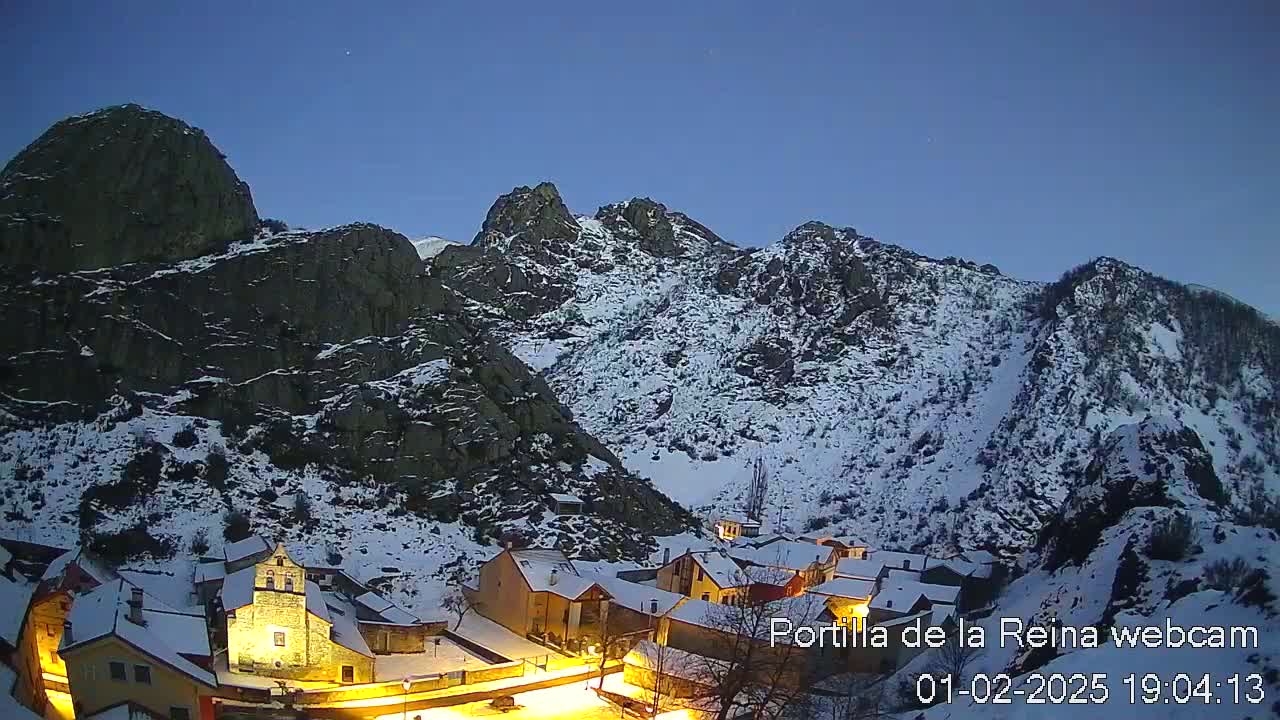 A snow-covered village nestled in a valley between dark, rocky mountains under a twilight sky.