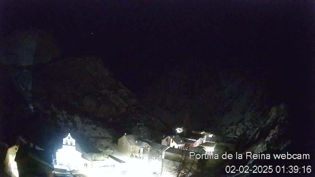 A nighttime view of a snow-dusted village nestled between dark mountains under a clear, starlit sky.