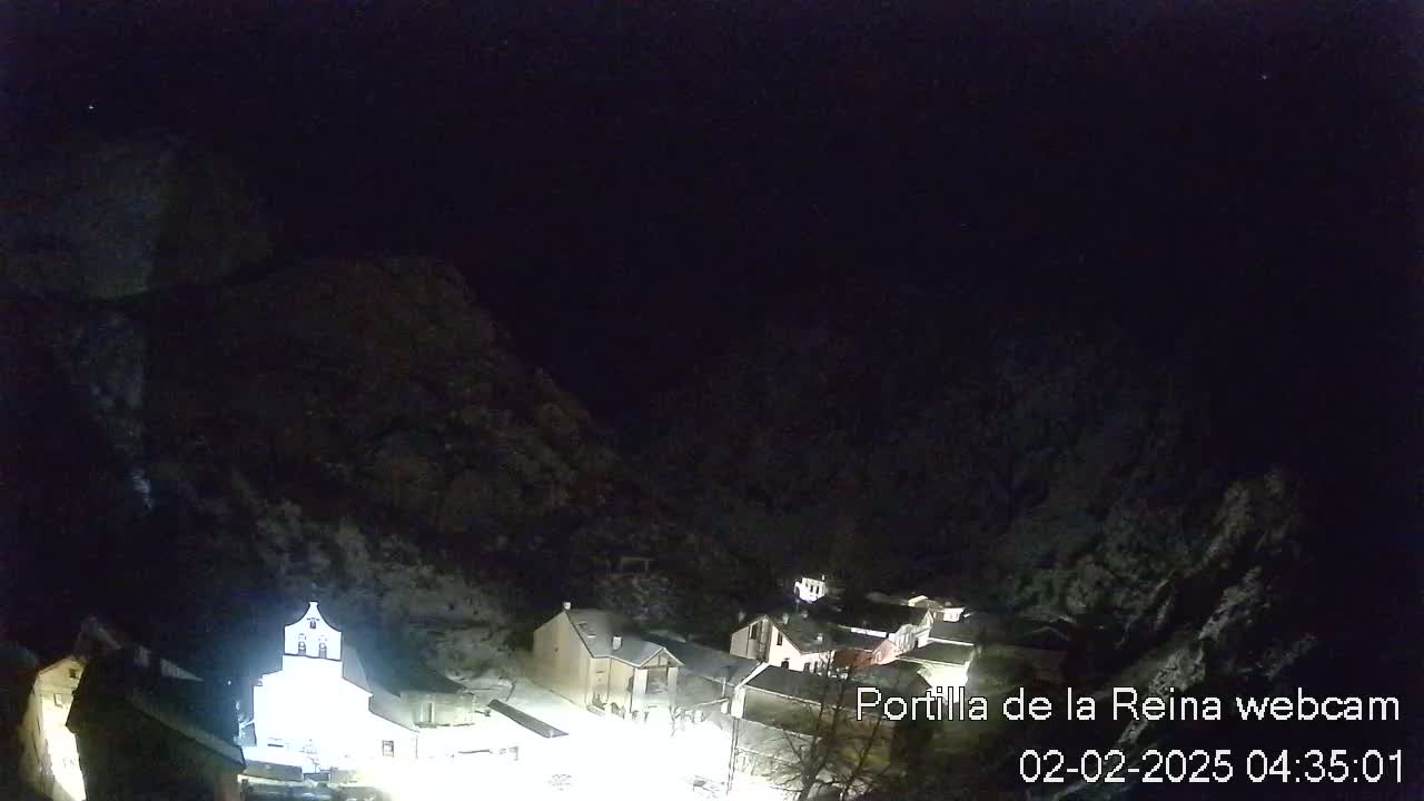 A snow-covered village nestled in a valley at night, illuminated by artificial light, under a dark sky.