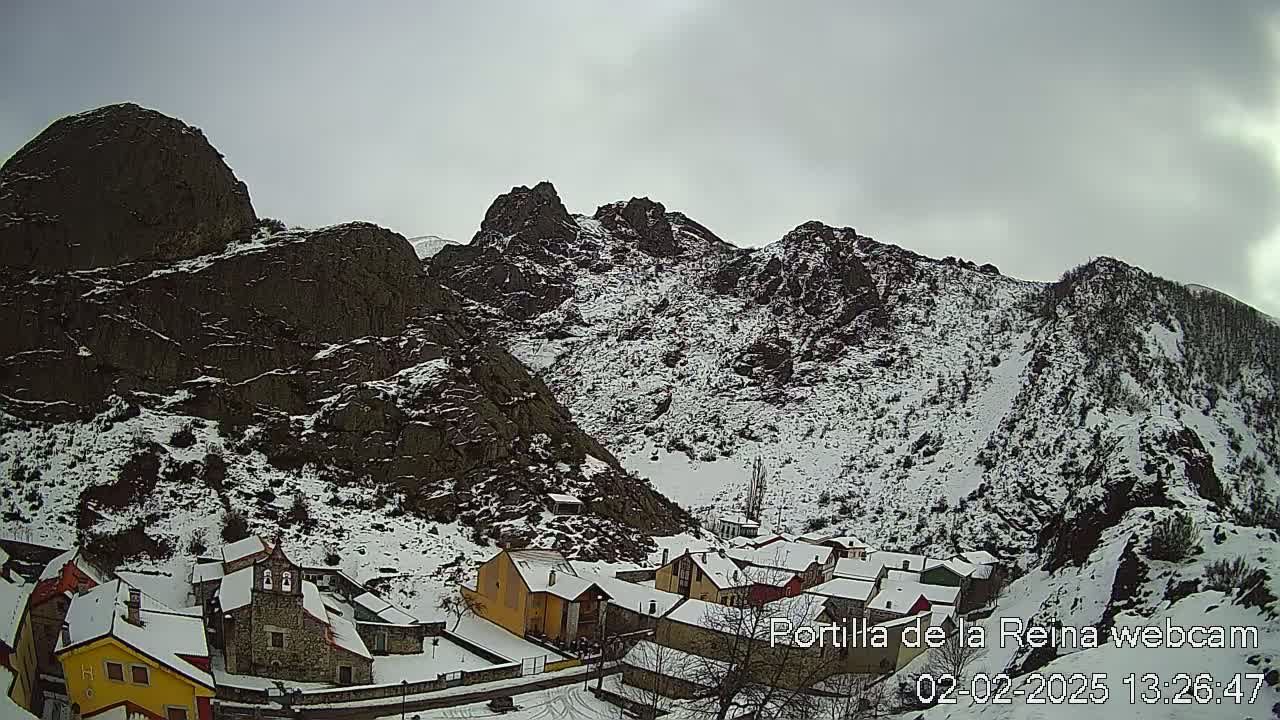 A snow-covered village nestled in a valley between rocky mountains under an overcast sky.