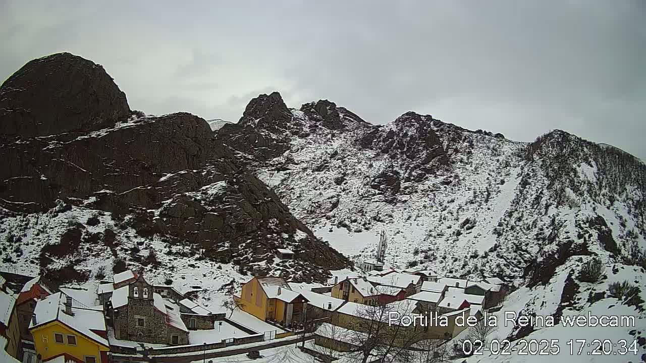 A snow-covered village nestled in a valley between dark, rocky mountains under an overcast sky.
