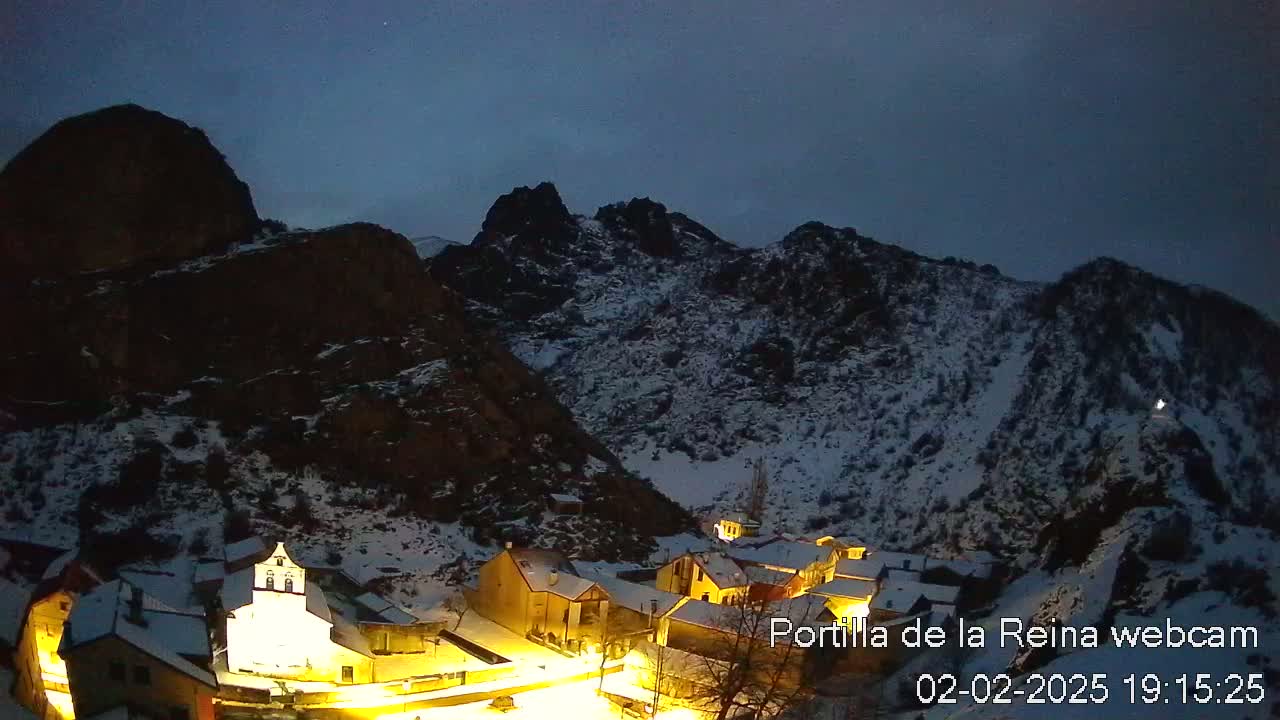 A snow-covered village nestled in a valley between dark, snow-dusted mountains under a twilight sky.