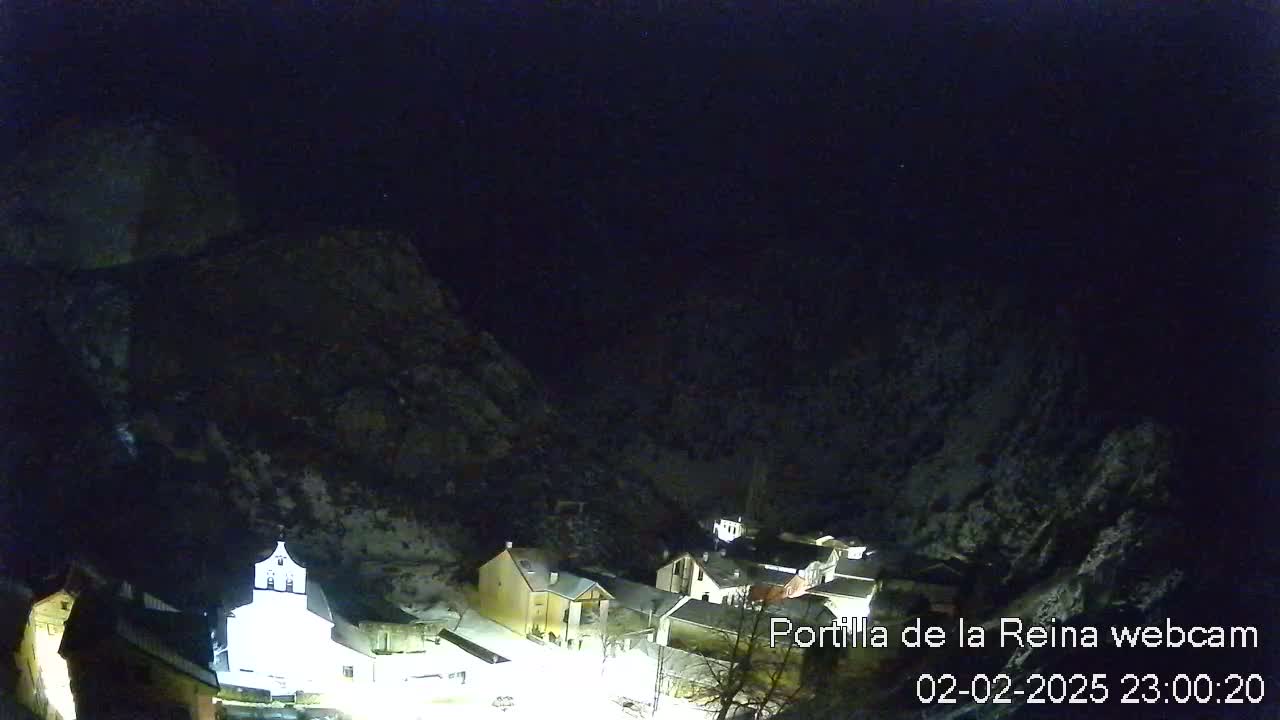 A nighttime view of a small village nestled in a snow-covered mountain valley under a clear, dark sky.
