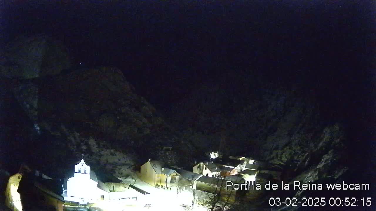 A nighttime view of a small village nestled in a snow-covered mountain valley under a dark, clear sky.