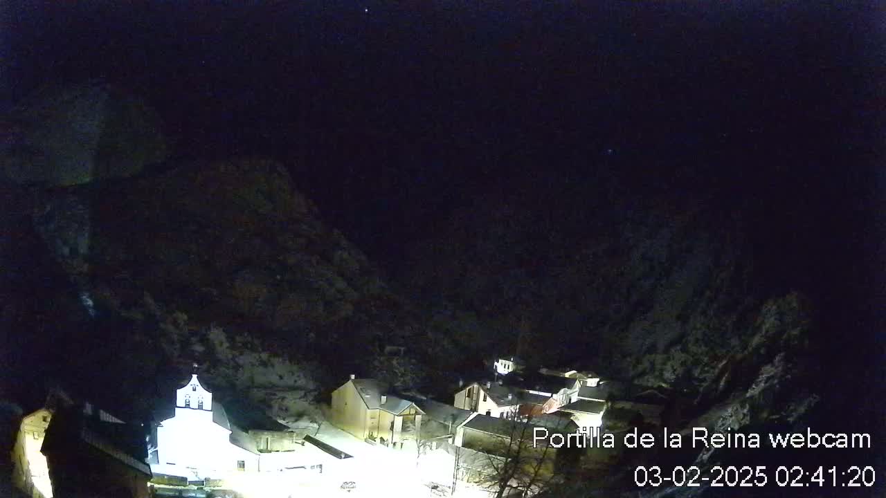 A nighttime, snow-dusted village nestled between dark, snow-covered mountains under a clear, starlit sky.