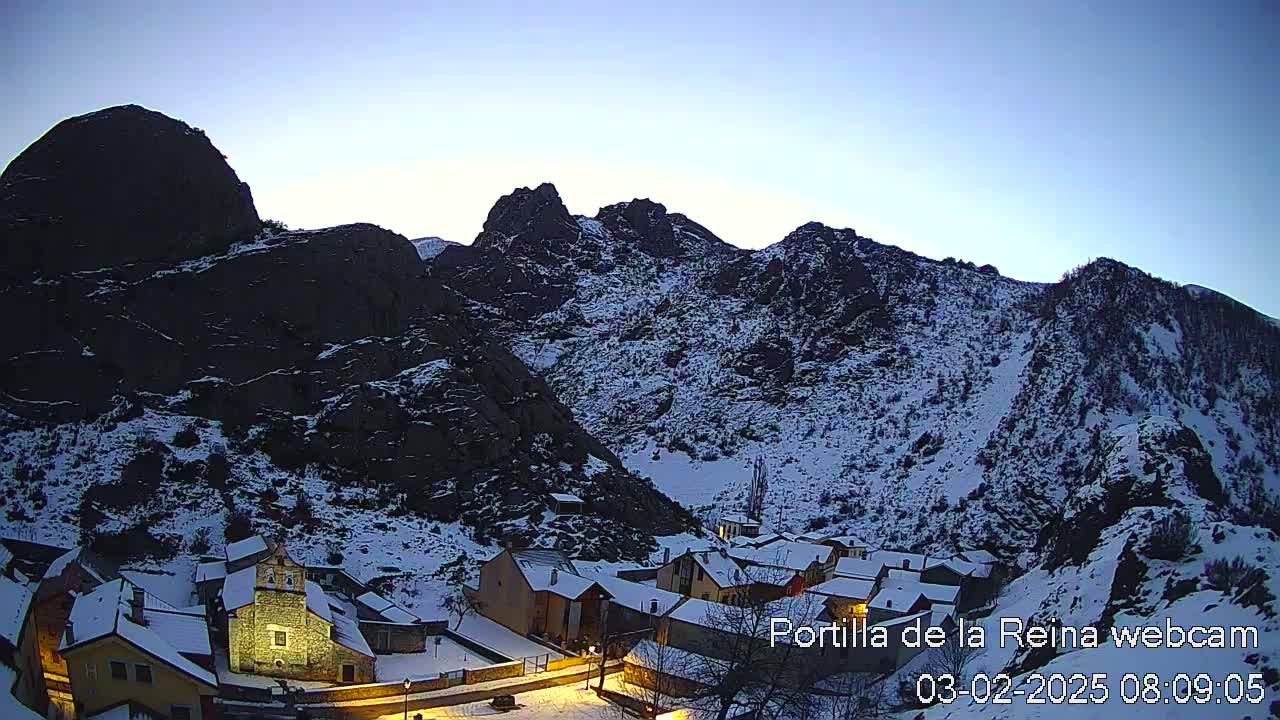 A snow-covered village nestled in a valley between dark, rocky mountains under a twilight sky.