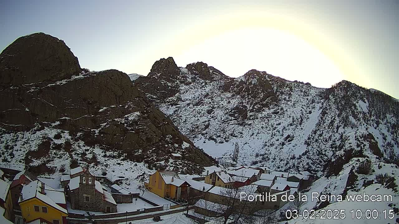 A snow-covered village nestled in a valley between rocky mountains under a bright, clear sky.
