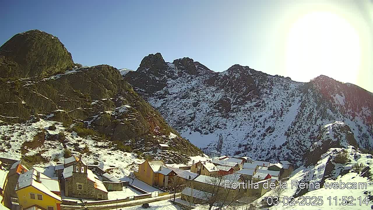 A small village nestled in a snow-dusted mountain valley under a bright, sunny sky.
