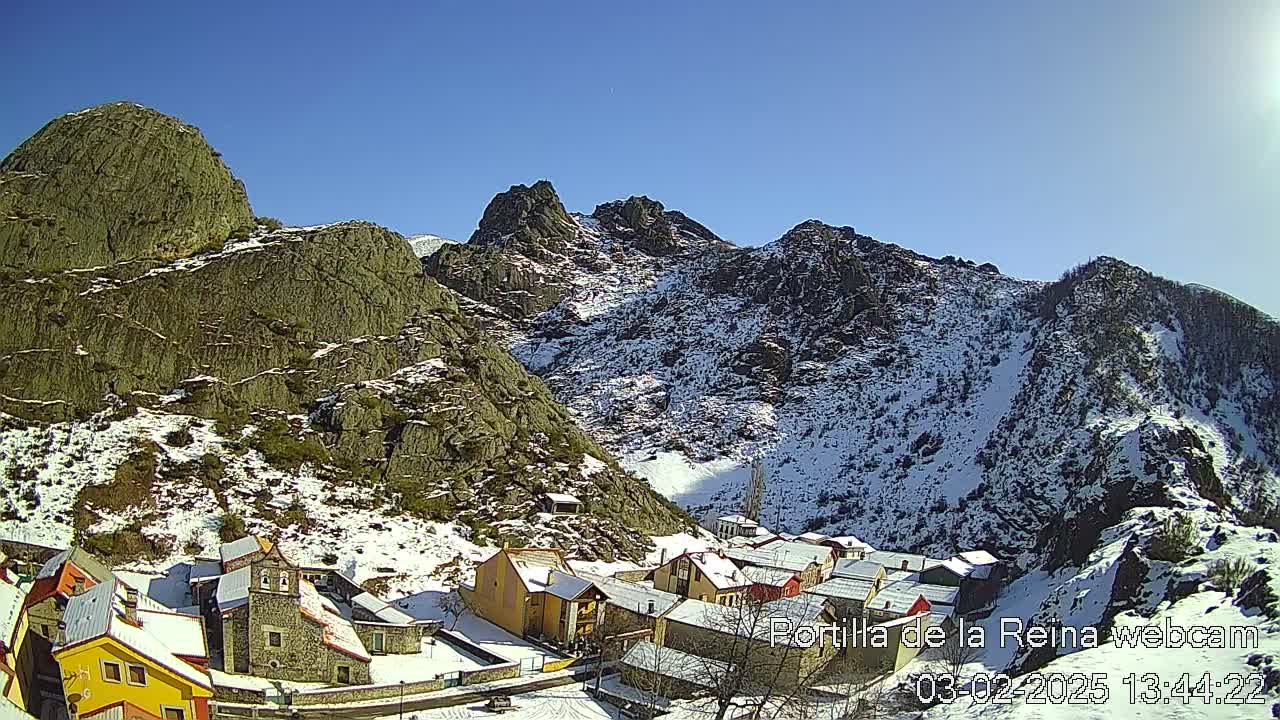 A snow-dusted mountain village nestled in a valley between rocky, snow-capped mountains under a clear blue sky.
