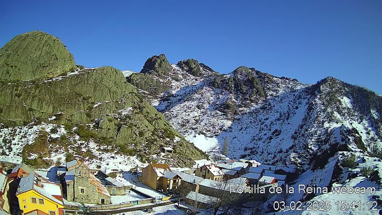 A small village nestled in a snow-dusted mountain valley under a clear blue sky.
